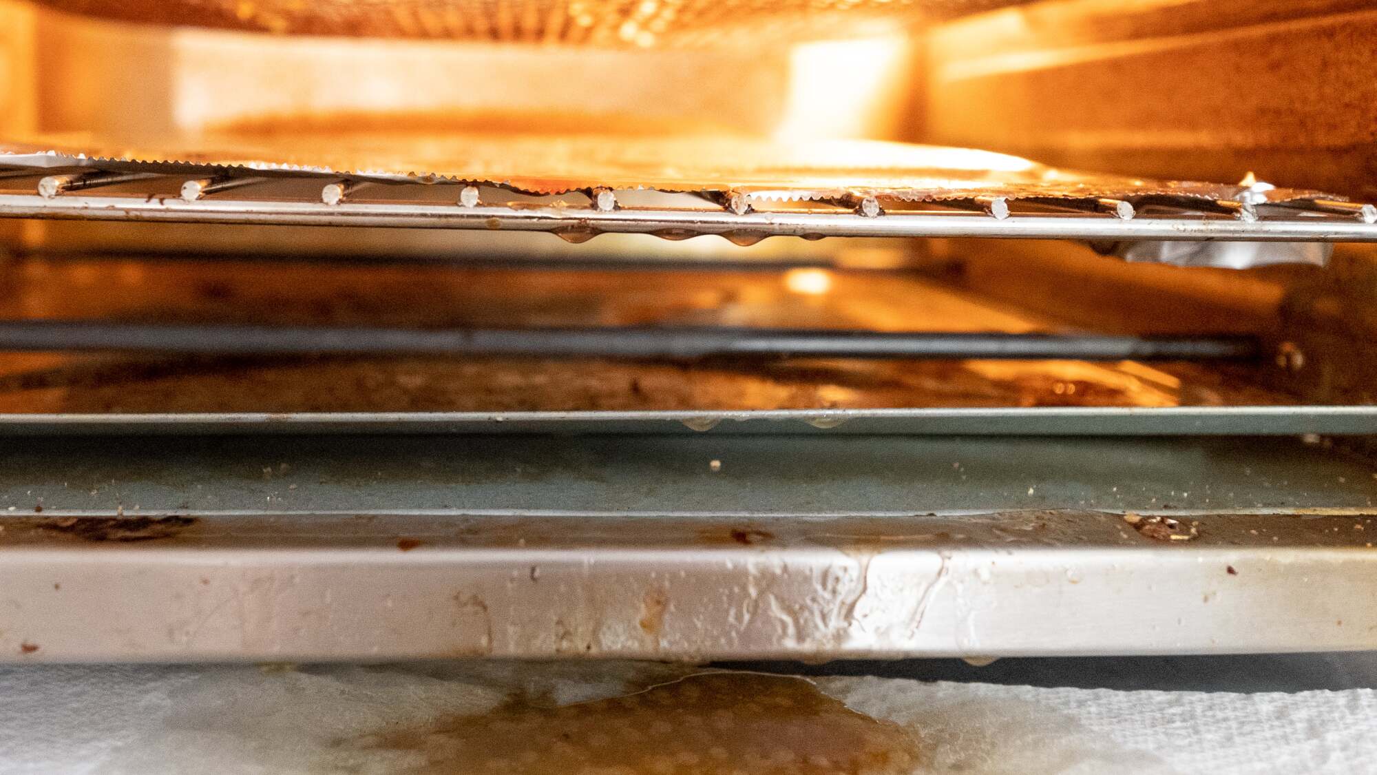 Front-facing photo of a countertop convection oven. There's grease dripping off the middle rack, bottom tray, and all the way out onto the counter. 