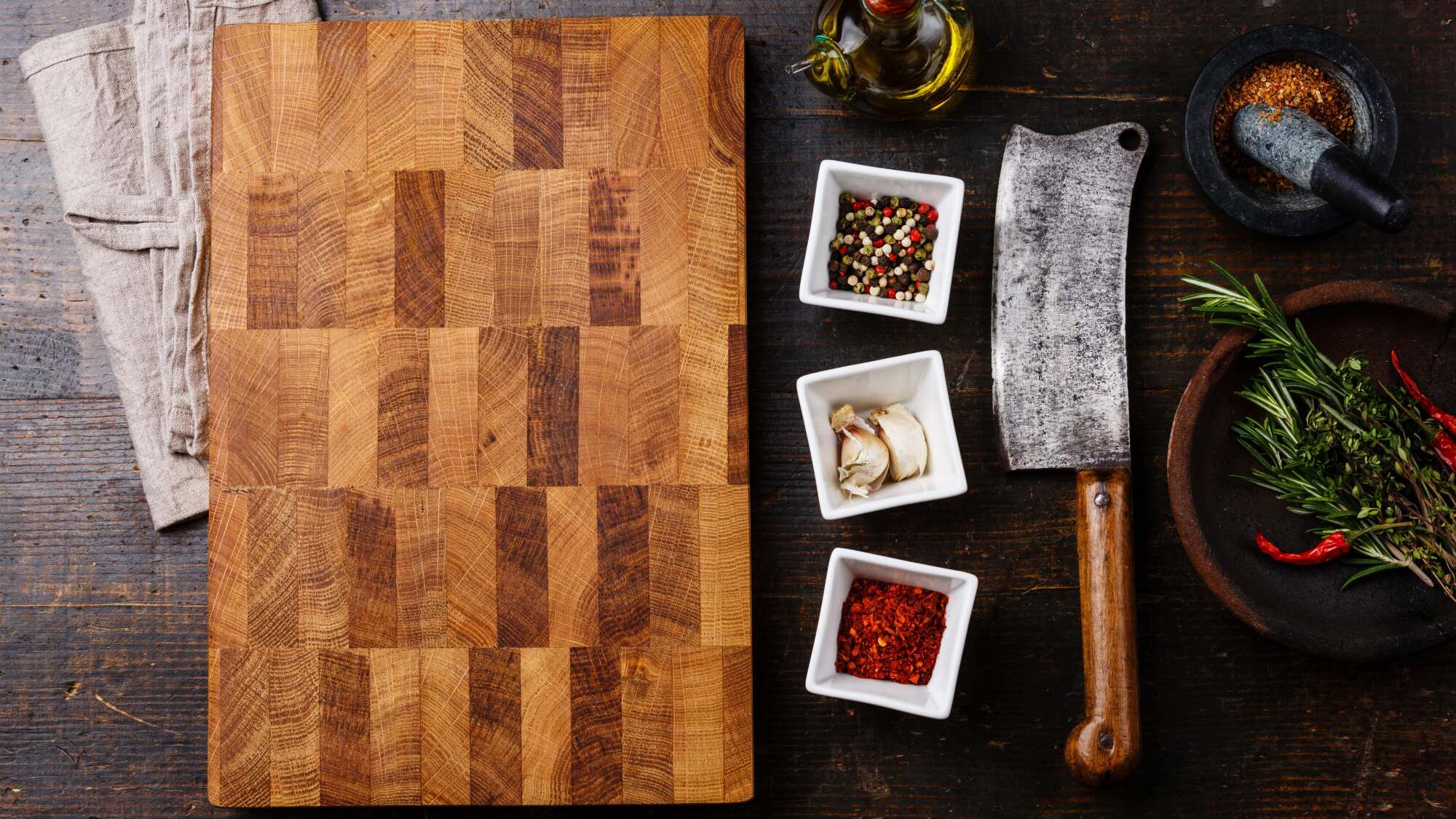 Large end-grain cutting board on a table with a cleaver and spices.