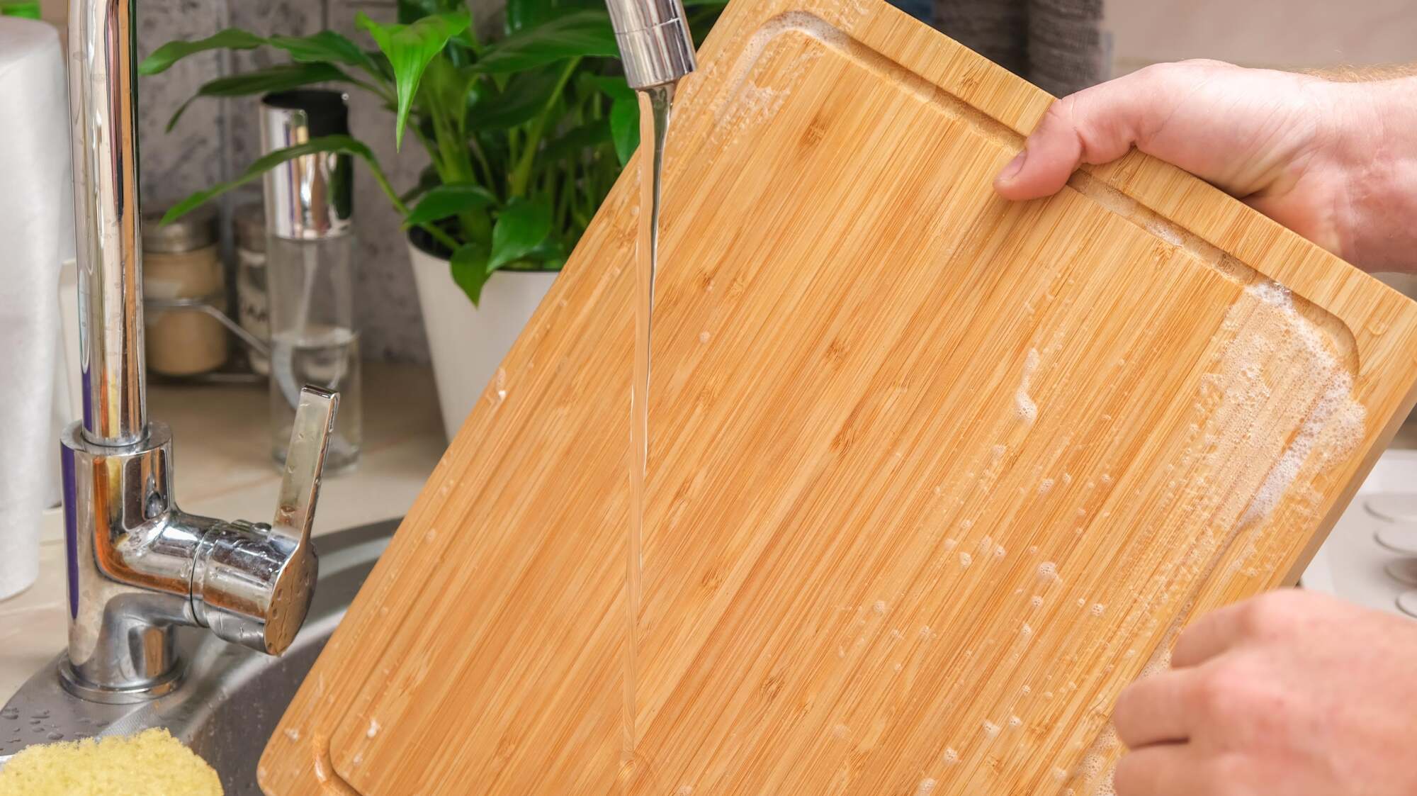 Hands washing a bamboo cutting board in the sink.