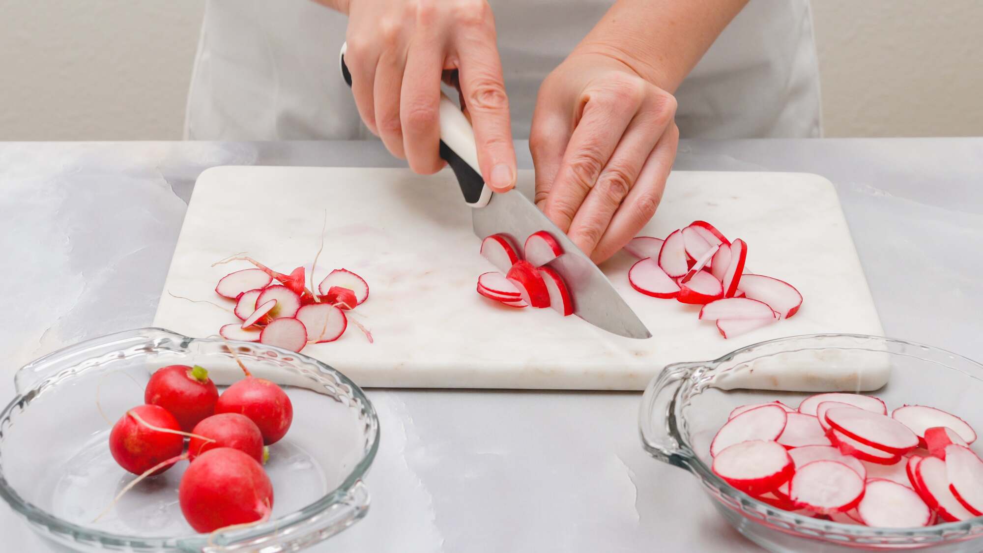 Hands cutting a radish on a marble cutting board.