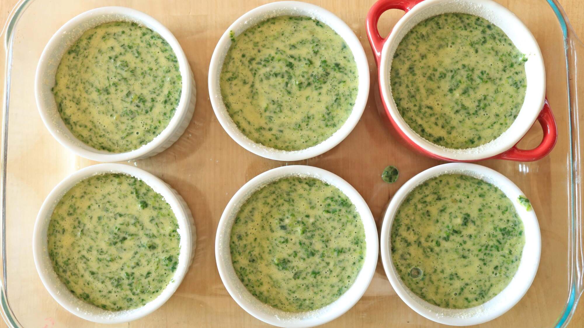 Ramekins in a casserole dish filled with spinach batter.