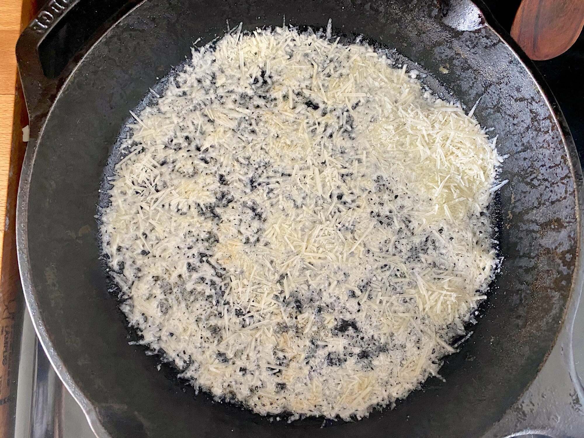 Cast iron skillet with shredded parmesan cheese sprinkled in an even layer onto the bottom.