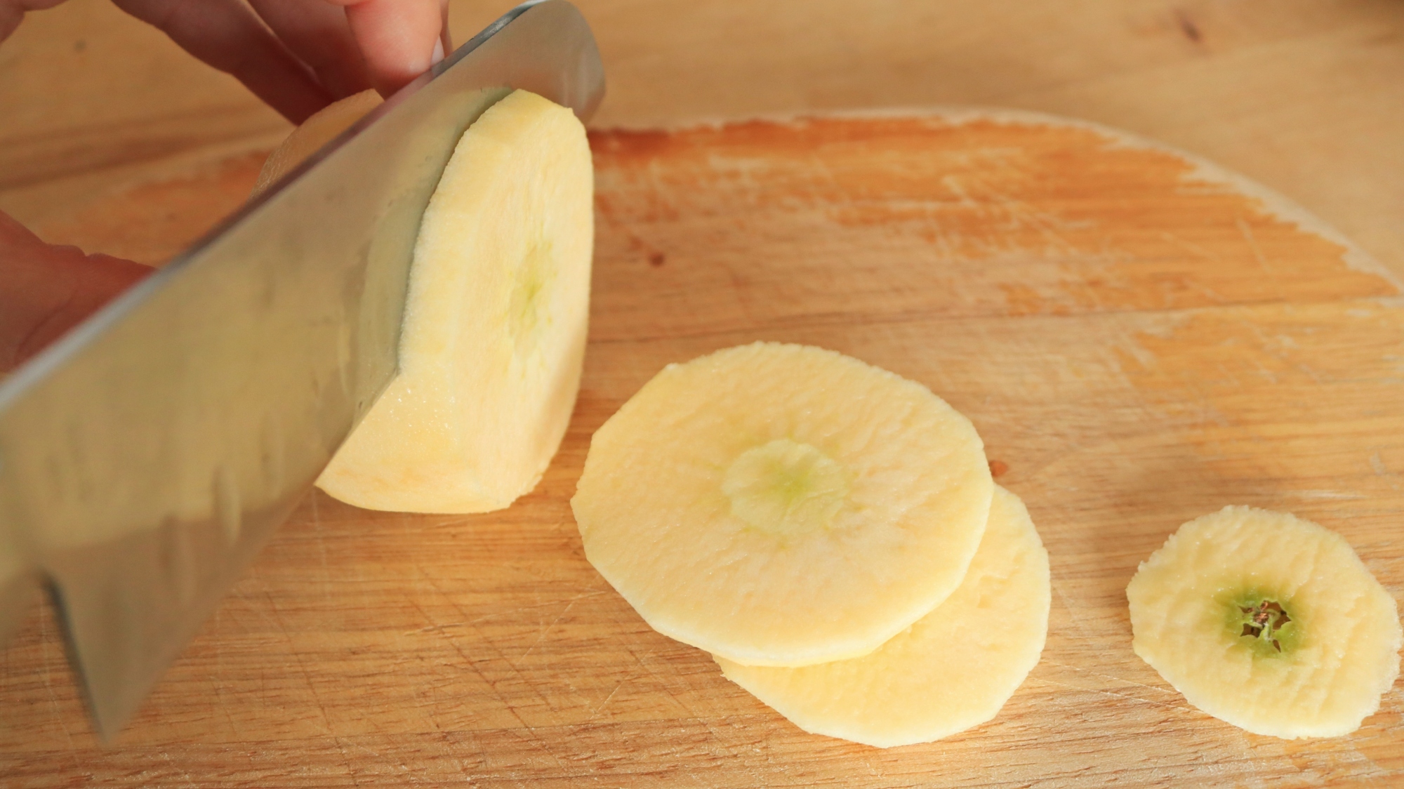 A knife slicing an apple on a cutting board.