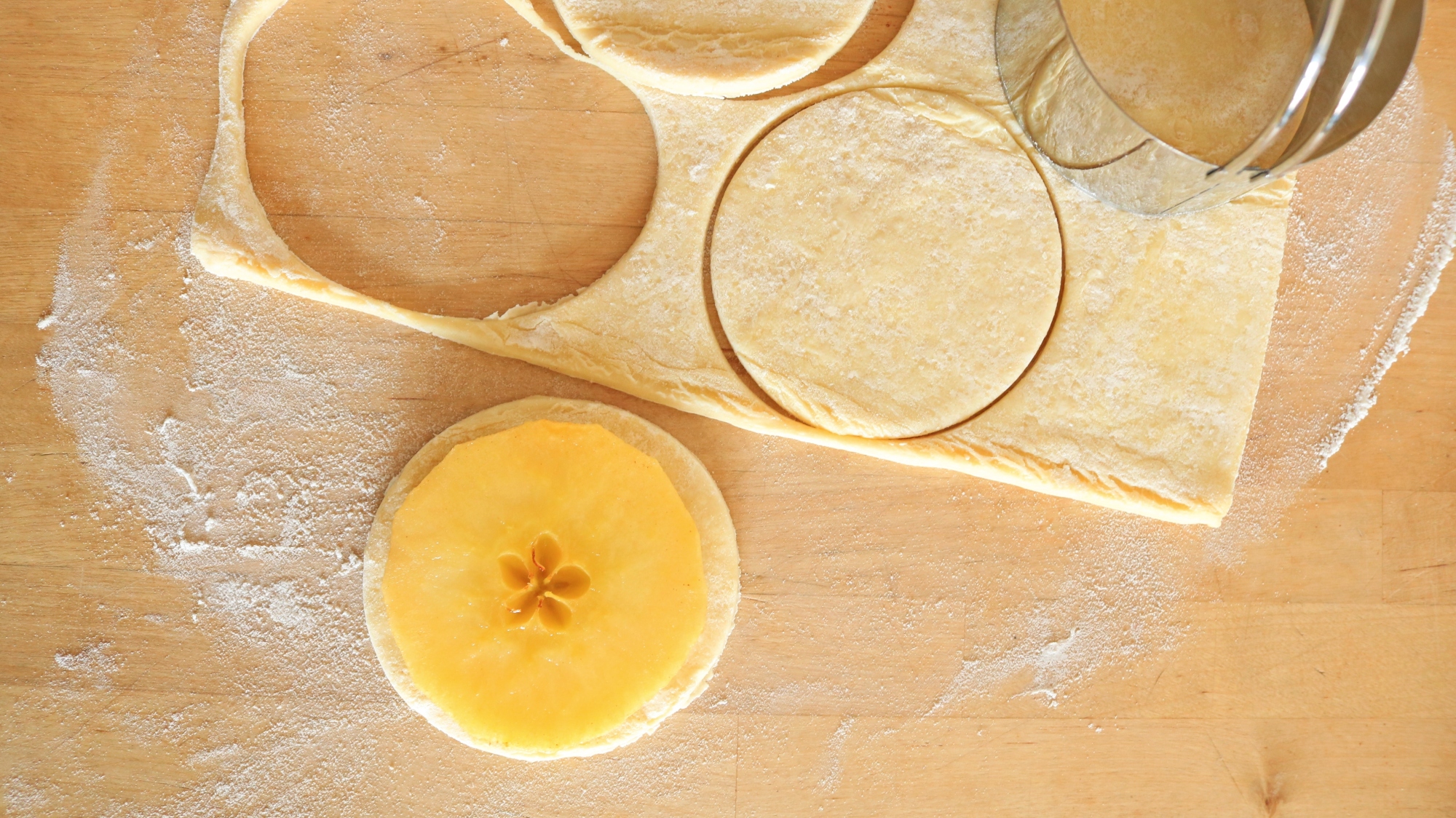 An apple slice on a circle of puff pastry near the pastry scraps.