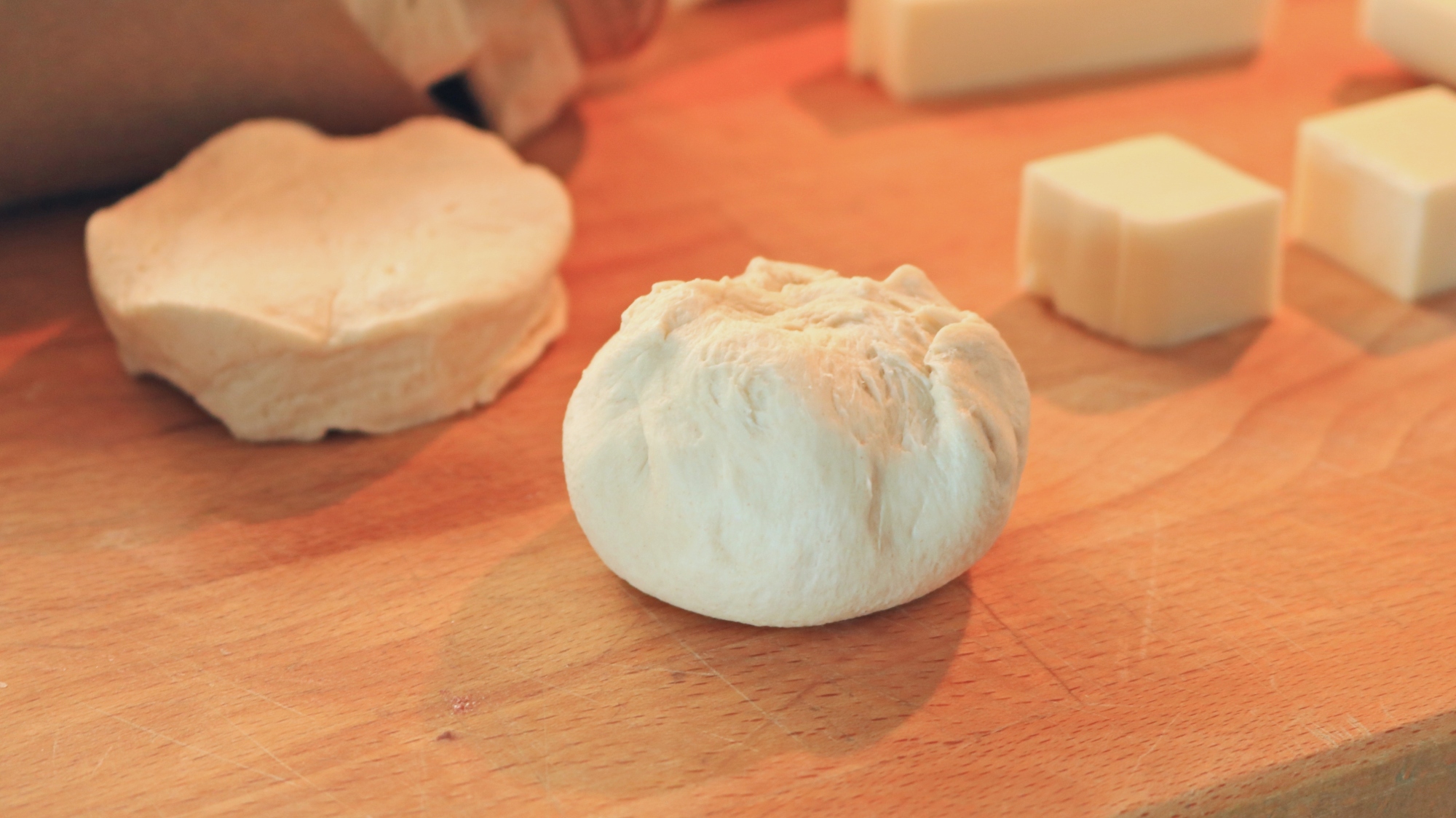 A biscuit ball next to cheese cubes and biscuit dough.