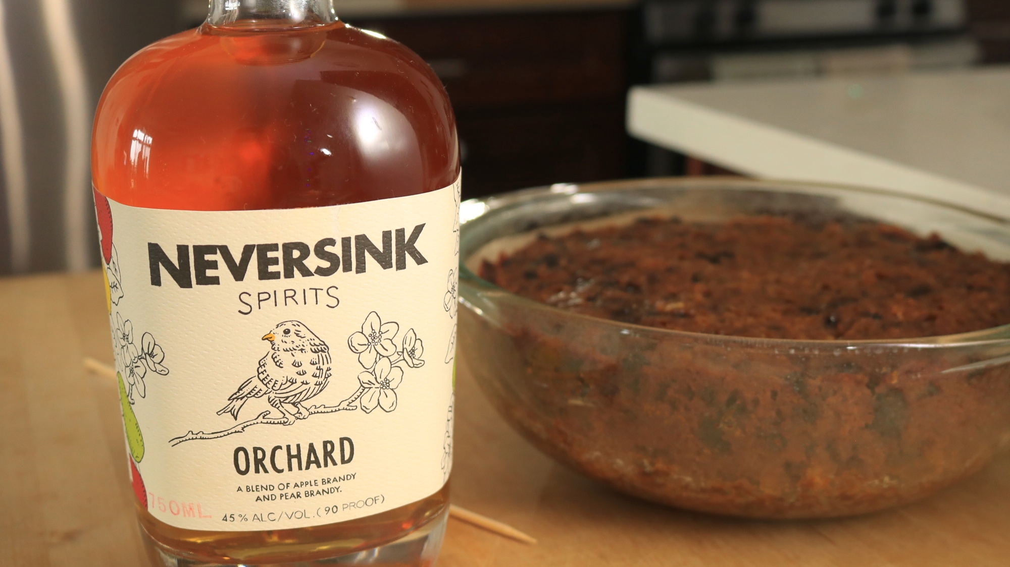 A bottle of brandy sits next to a cake in a bowl.