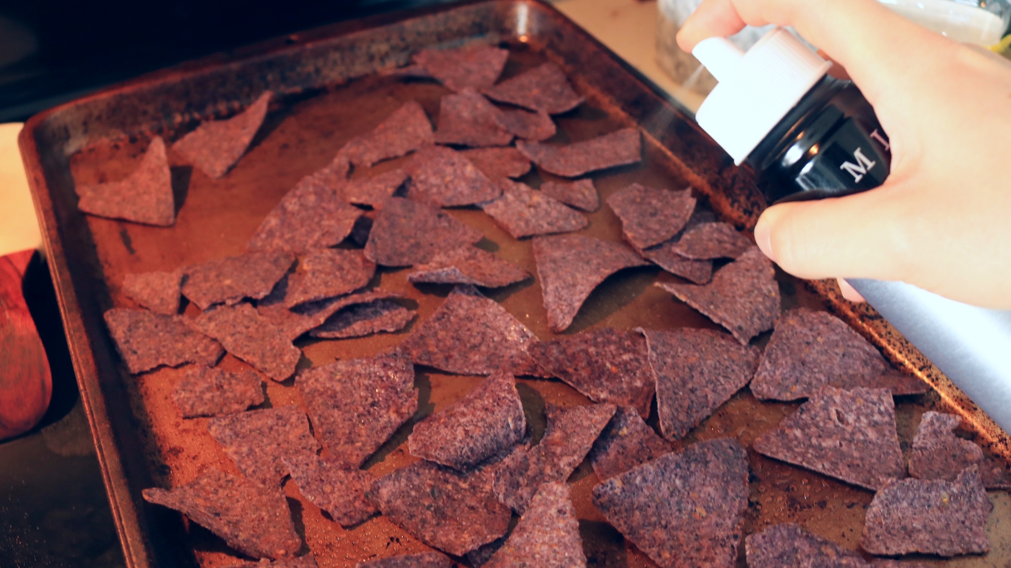 Hand using spray bottle to spray liquid onto blue corn chips.