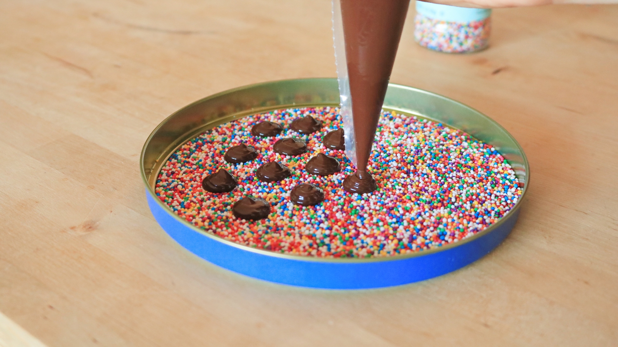 Piping bag making chocolate circles in a dish of sprinkles.