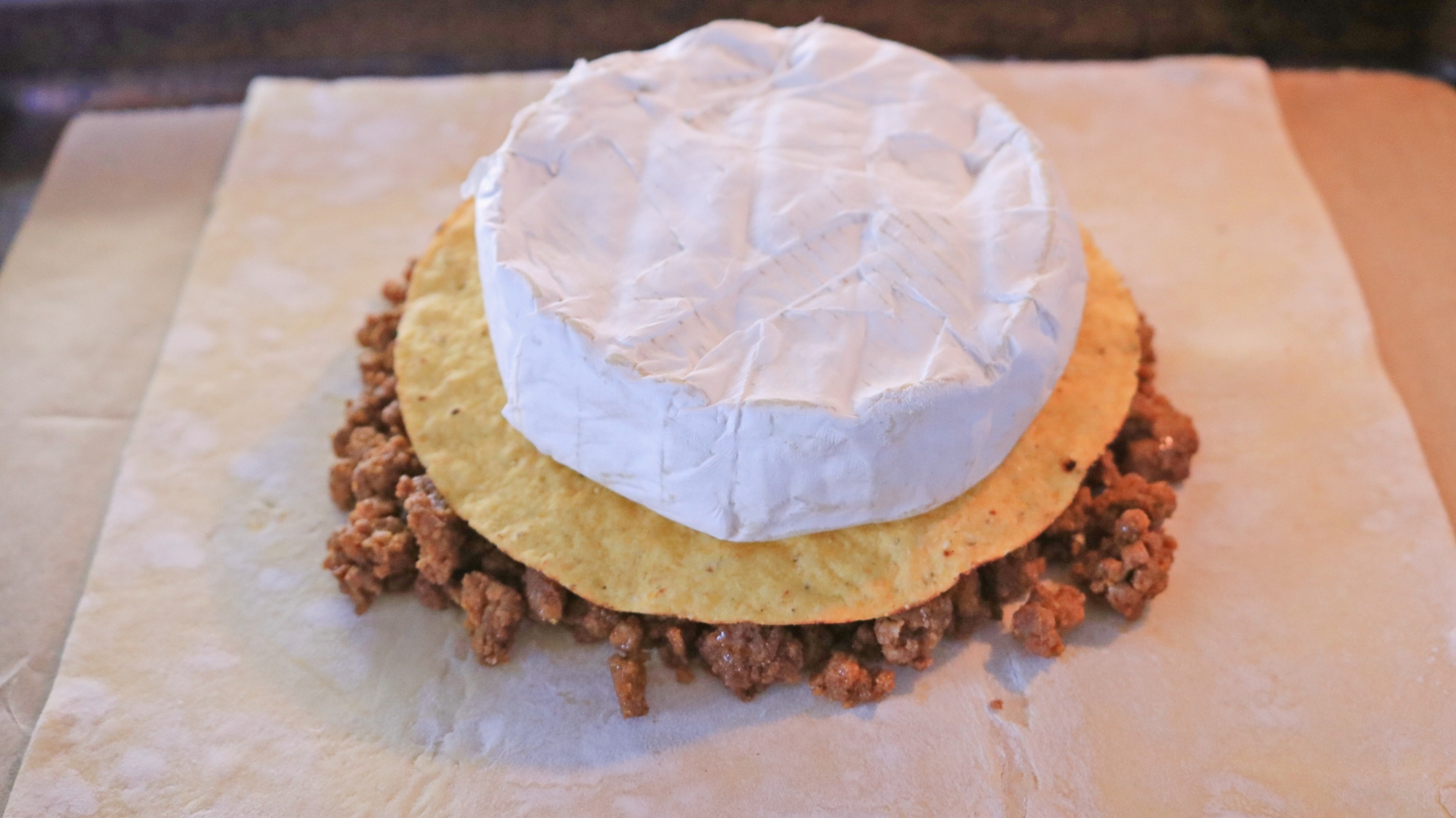 A wheel of brie on top of a tortilla and ground beef on puff pastry.