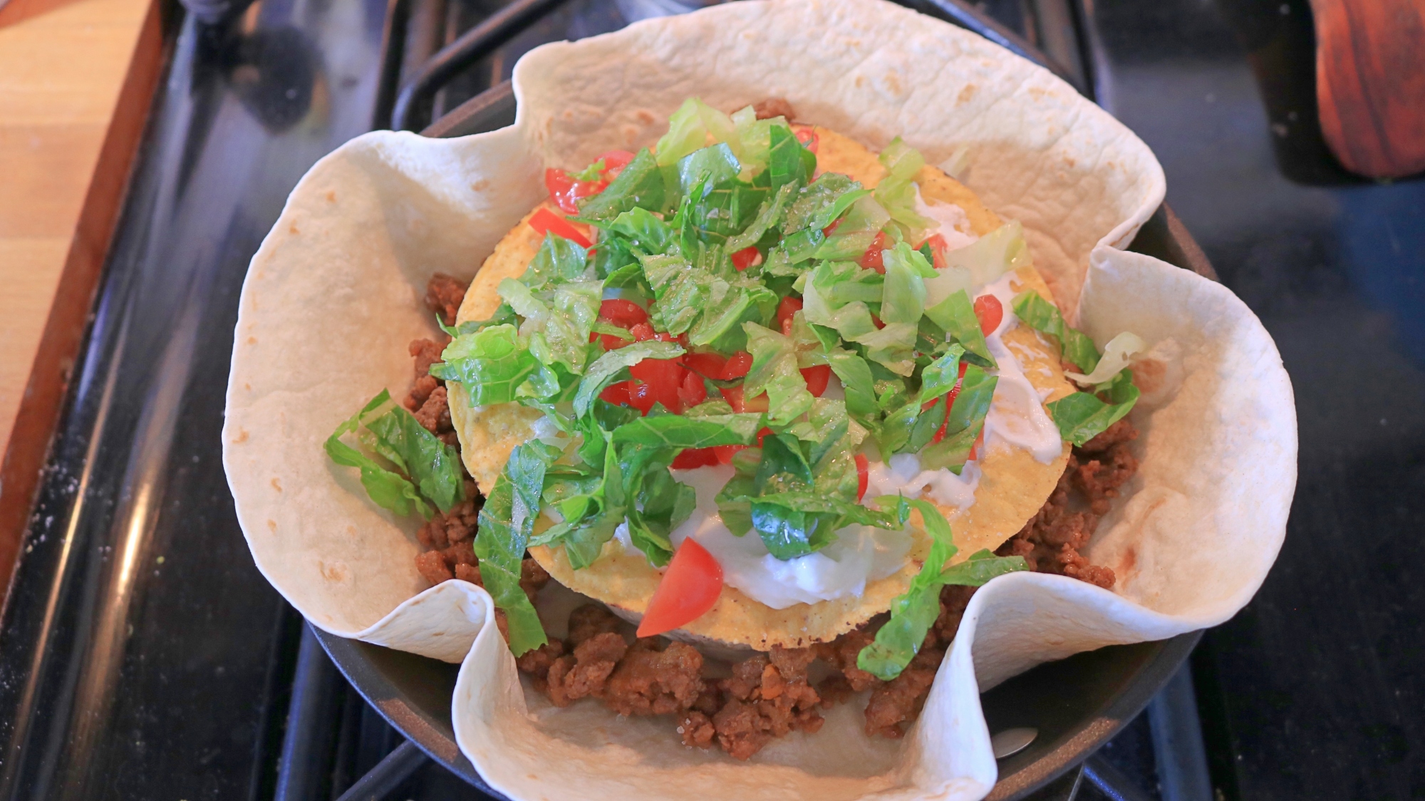 A flour tortilla with beef, brie, yellow tortilla, lettuce, and tomato in a frying pan.