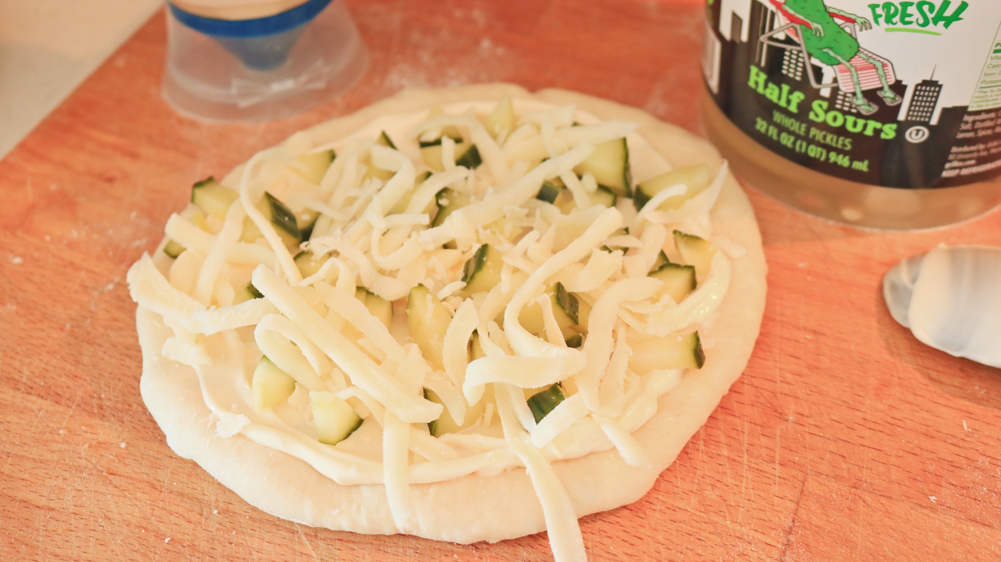 Pickles and cheese on a mayonnaise coated pizza crust.