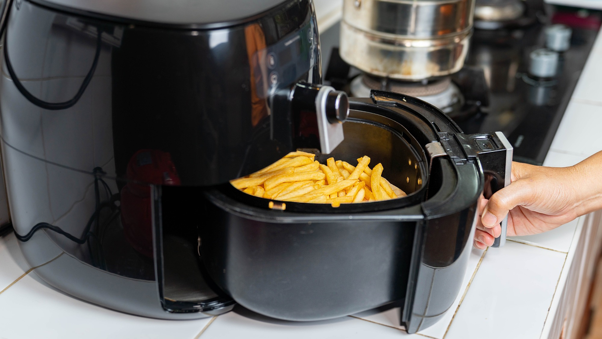 Hand opening air fryer basket full of french fries.