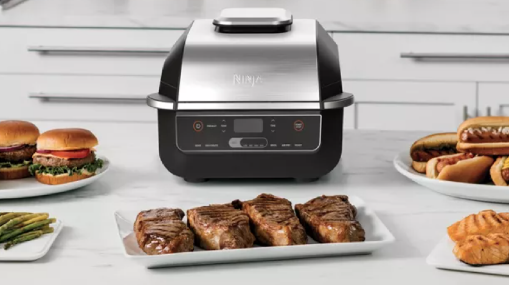 A grill style air fryer on a counter with plates of food.