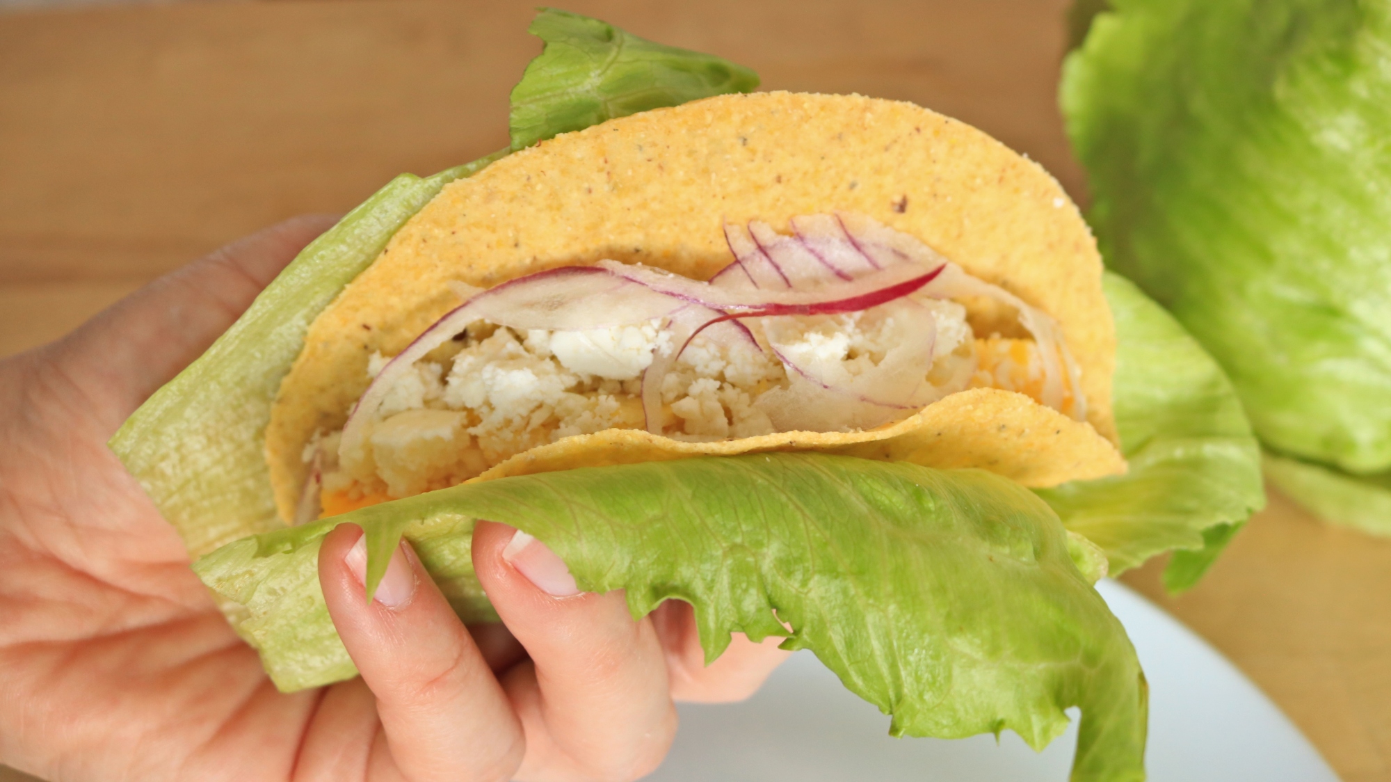 Hand holding a leaf of lettuce around the outside of a taco.