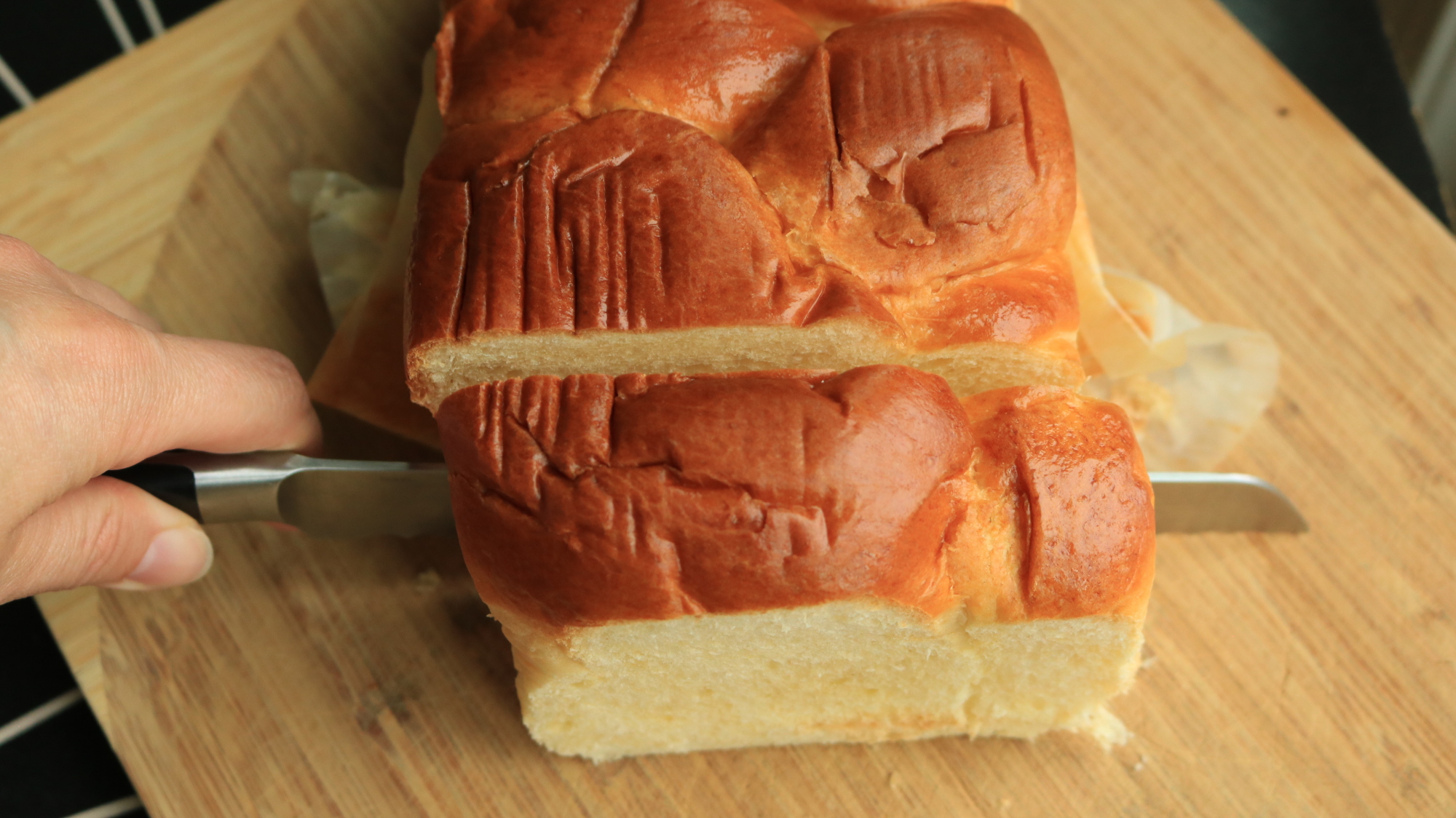 A knife slicing a wide piece of bread from the rest of the loaf.