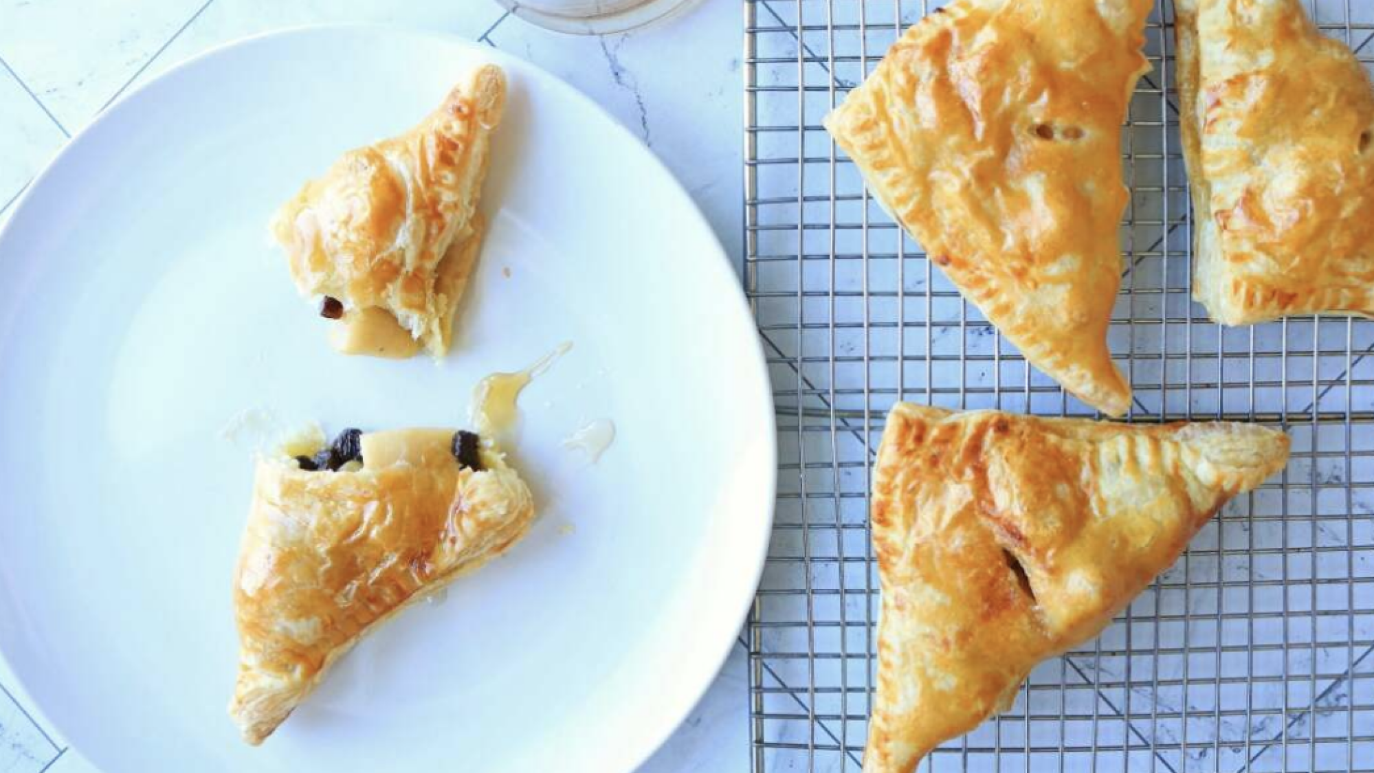 A broken apple turnover on a plate next to others on a wire rack.