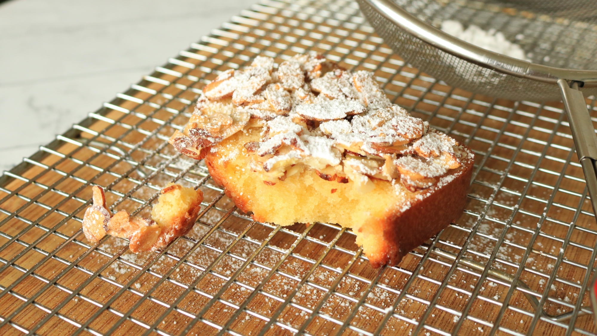 Pound cake with almond topping with a piece broken off.