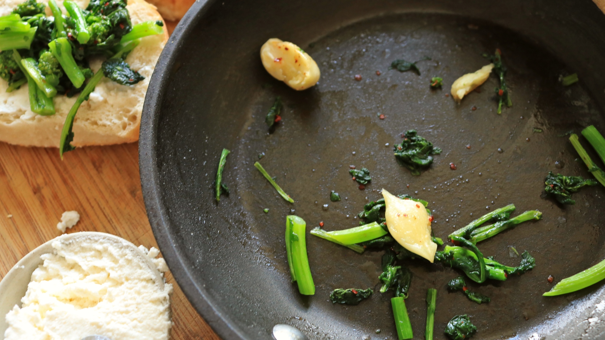 A pan with broccoli rabe pieces and garlic strewn about.