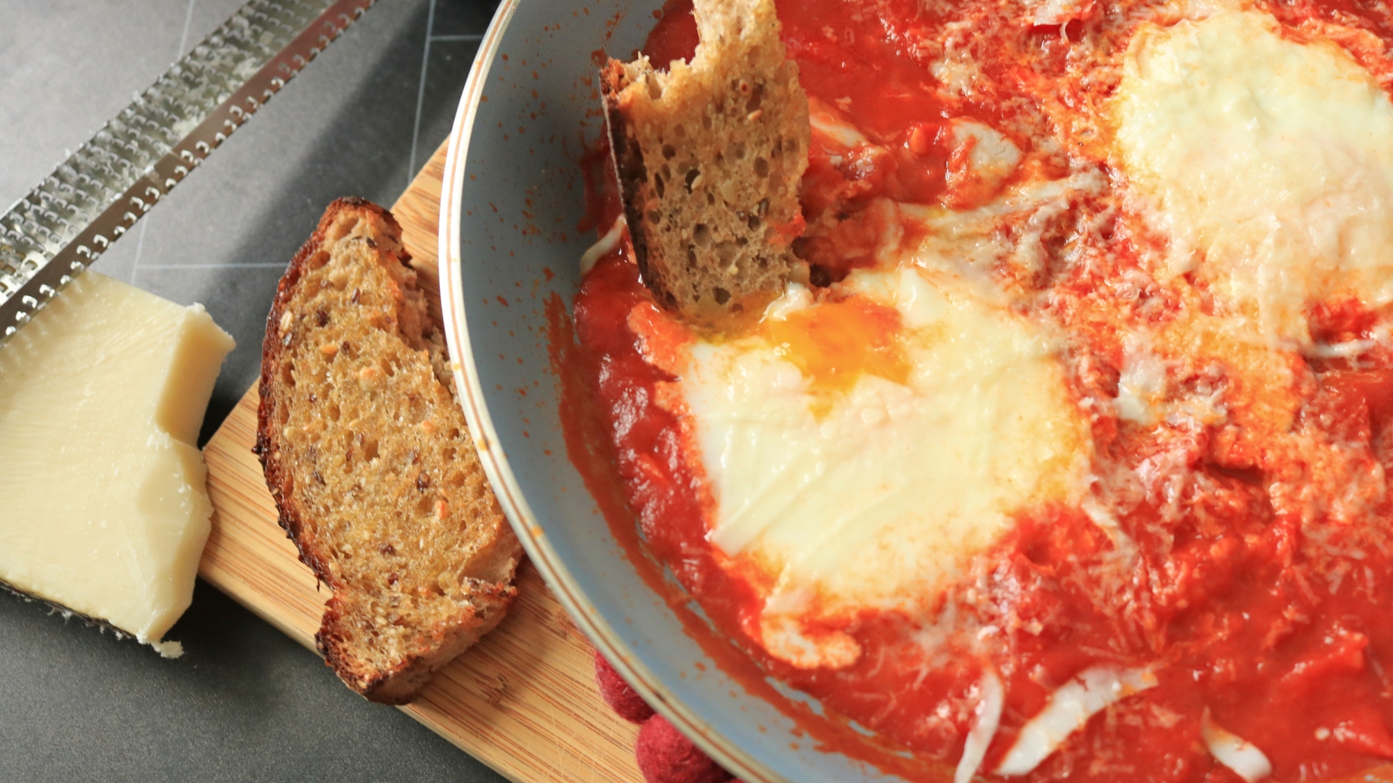 Close up of a pan of eggs and tomatoes next to torn bread.