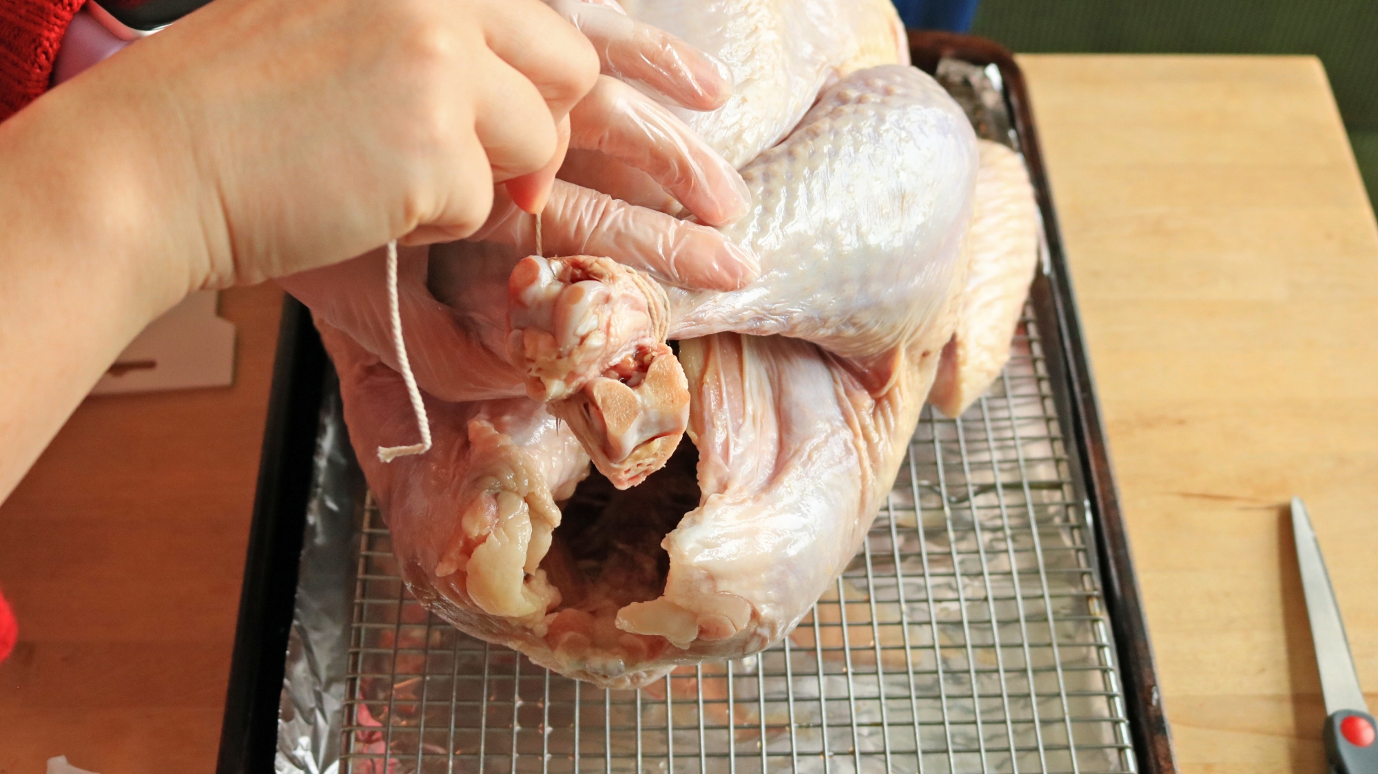 A hand wrapping kitchen string around the turkey's legs.