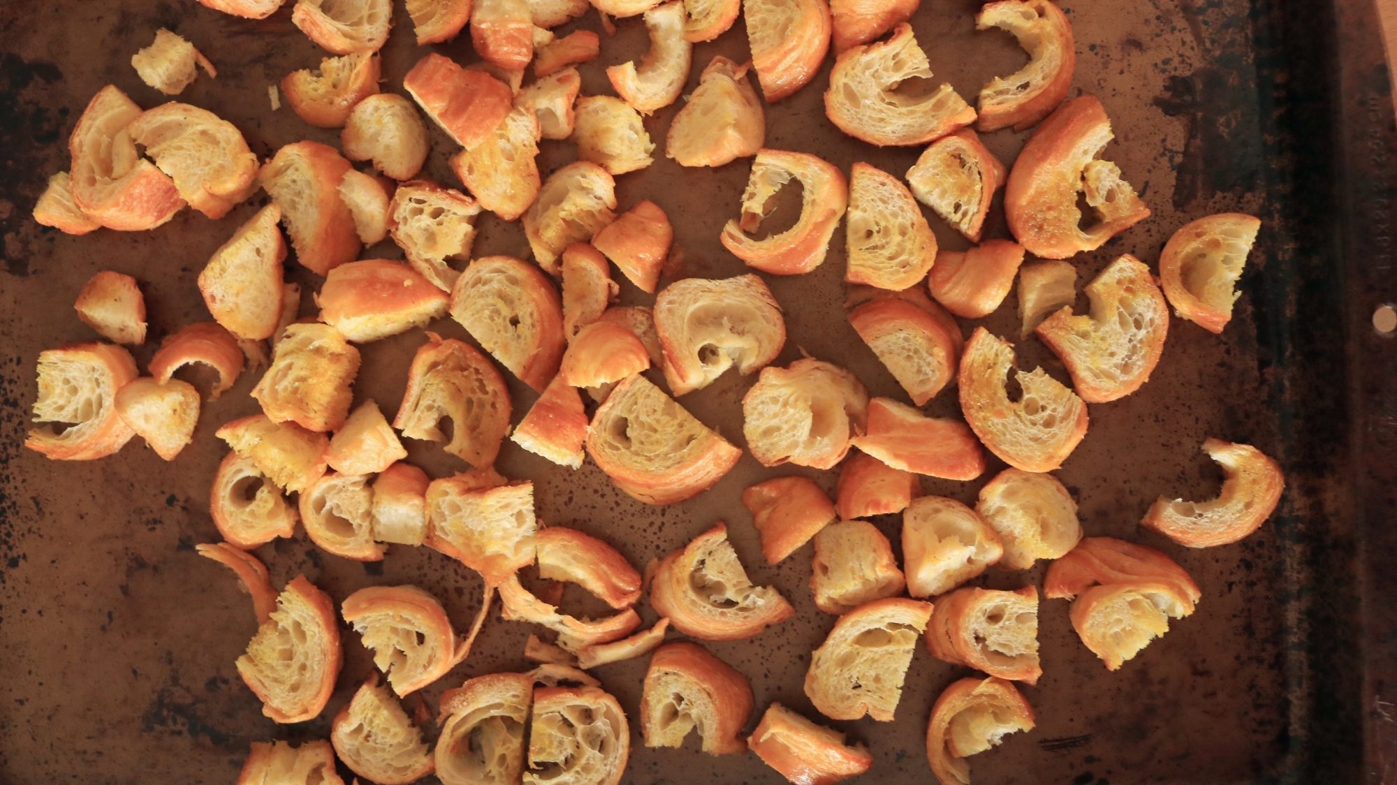 Croissant pieces spread out on a sheet tray.